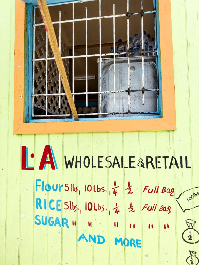 Hand painted sign: LA Wholesale & Retail with prices of Flour, Rice, Sugar and more.