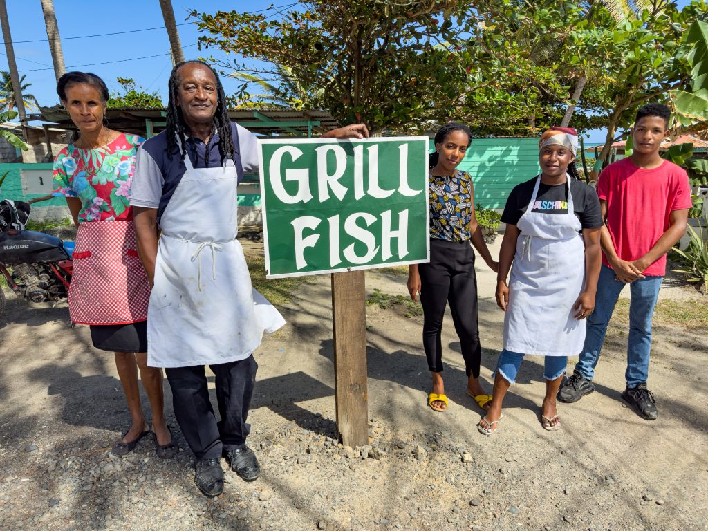 The family who cooked wonderful grilled fish just minutes away from the airport in St. Lucia standing next to Grill Fish sign.